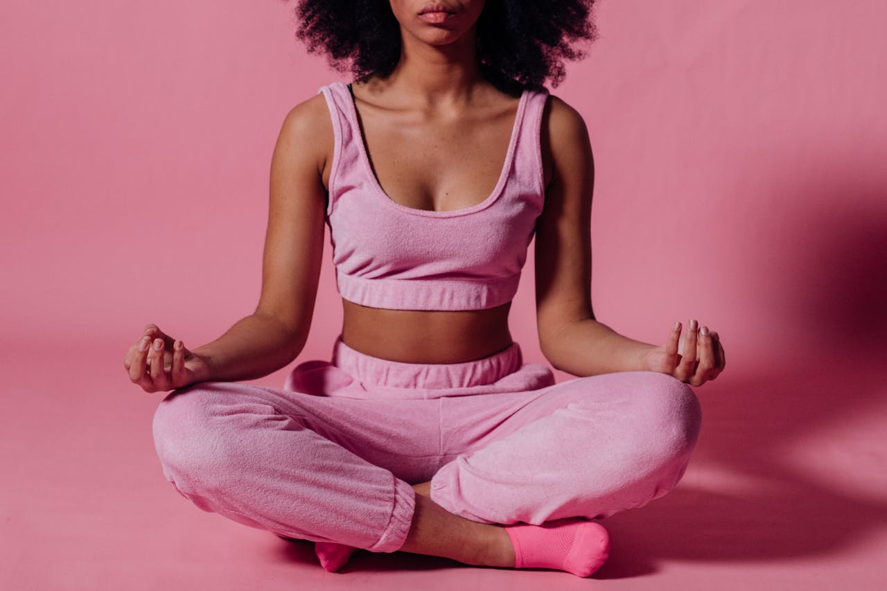 Young woman meditating in studio, embracing calmness and wellness in a pink outfit.